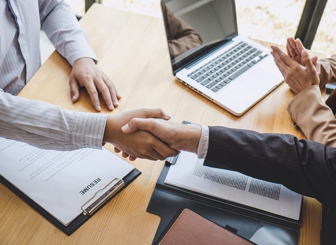 Join Our Team - Closeup View of a Manager Shaking Hands with a New Job Applicant During an Interview with a Portfolio Resume and Laptop on the Table